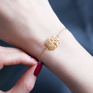 May include: A gold chain bracelet with a monogram charm. The charm is a delicate, cursive script of three letters.