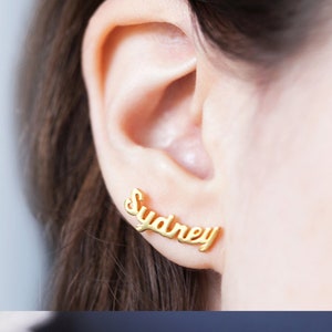 May include: Gold-toned earrings with the name "Sydney" spelled out in a cursive font.