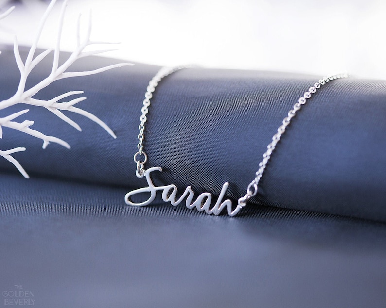 Op de afbeelding: Een zilveren ketting met de naam "Sarah" in cursief schrift.