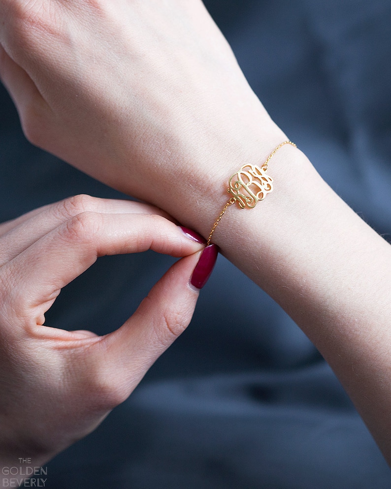 May include: A gold chain bracelet with a monogram charm. The charm is a delicate, cursive script of three letters.