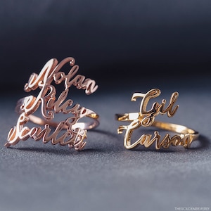 May include: Two gold rings with names engraved on them. The ring on the left has the names "Nolan", "Riley", and "Scarlett" engraved on it. The ring on the right has the names "Gyl" and "Carson" engraved on it.