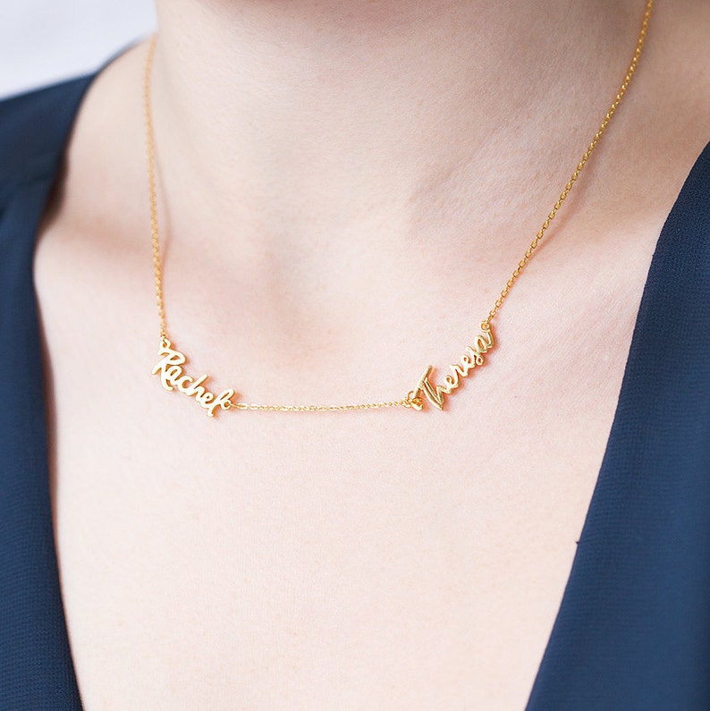 Op de afbeelding: Een gouden ketting met twee namen, "Rachel" en "Teresa", geschreven in cursief.
