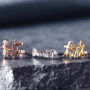 May include: Three personalized rings with names written in cursive. The rings are made of silver, gold, and rose gold. The names on the rings are "Payton Hayden", "Charlotte", and "Emily Matthews".