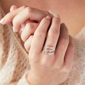 May include: A silver ring with three names engraved on it: Adrian, Karizma, and Seraphina.