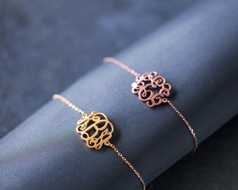 May include: Two delicate gold and rose gold chain bracelets with monogrammed charms. The charms are in a script font and feature three letters each.