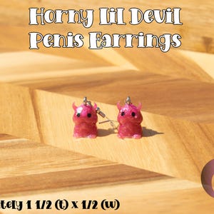 May include: A pair of pink glittery resin earrings shaped like small devil figures with horns and black eyes. The text "Horny Lil Devil Penis Earrings" is at the top, and "approximately 1 1/2 (t) x 1/2 (w)" is at the bottom.