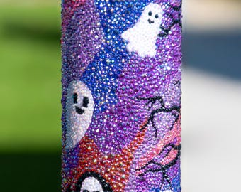 May include: A Halloween-themed, bedazzled 15 oz tumbler with a black lid. The tumbler is covered in iridescent rhinestones in shades of purple, blue, and red. White ghost and a black Grim Reaper designs are featured on the tumbler.