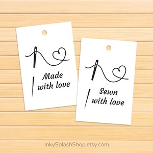 Puede incluir: Dos etiquetas rectangulares blancas con un dise&ntilde;o de aguja e hilo, una que dice "Made with love" y la otra "Sewn with love". Las etiquetas tienen un peque&ntilde;o agujero en la parte superior y est&aacute;n sobre un fondo de madera marr&oacute;n claro.