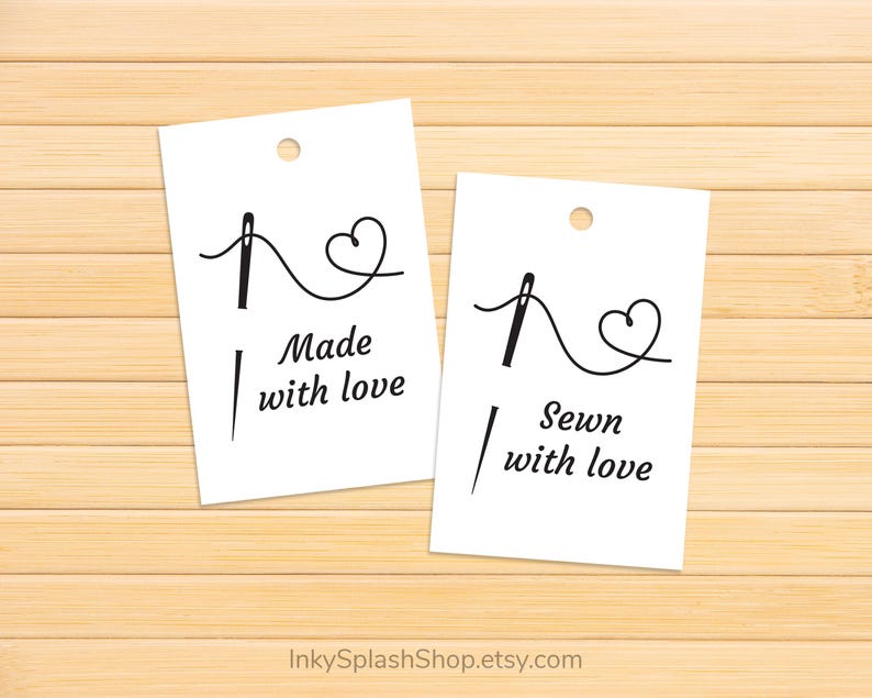 Puede incluir: Dos etiquetas rectangulares blancas con un dise&ntilde;o de aguja e hilo, una que dice "Made with love" y la otra "Sewn with love". Las etiquetas tienen un peque&ntilde;o agujero en la parte superior y est&aacute;n sobre un fondo de madera marr&oacute;n claro.