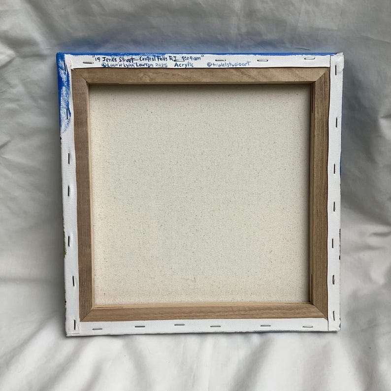 May include: A close-up of the back of a stretched canvas painting. The canvas is white and the frame is made of wood. The painting is titled "19 Jenks Street - Central Falls RI 9:09 am" and is signed "Lourive Lynn Lowton 2025 Acrylic" with the social media handle "@triplelstudioart" in the bottom right corner.