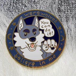 Op de afbeelding: Twee ronde emaille pins met een cartoon weerwolf ontwerp. De pins hebben een blauw en goud kleurenschema met de woorden "werewolves" en "believe in me". De wolf is grijs en wit, met de tekst "You can do it!"