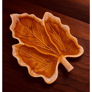 May include: A ceramic leaf-shaped serving dish with a brown glaze. The dish has a detailed leaf design and is perfect for serving snacks or appetizers.