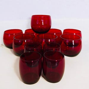 May include: A set of 10 red glass tumblers. The glasses are round and have a wide base. They are arranged in a pyramid shape.