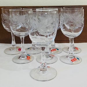 May include: Set of six clear glass stemmed wine glasses with an etched floral design. The glasses have a delicate, elegant look and are perfect for serving wine or other beverages.