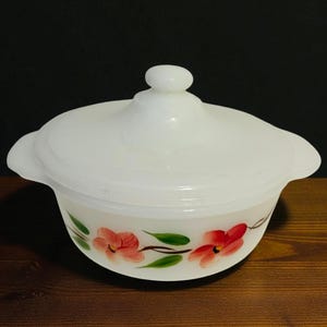 May include: A white, lidded serving bowl with a floral design. The bowl features a rounded shape with two handles and a knob on the lid. Red flowers and green leaves are painted around the base of the bowl.