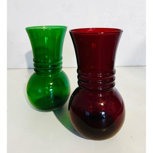 Peut inclure: Deux vases en verre, un vert et un rouge, sont présentés. Les vases ont une base arrondie, une section médiane côtelée et un sommet évasé. Le vase vert est à gauche et le vase rouge à droite.
