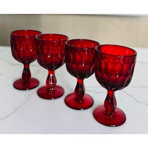 May include: A set of four ruby red glass goblets featuring a textured hobnail pattern on the bowl, a short stem, and a circular base. Each goblet has a deep red translucent finish and a consistent design with a rounded rim and a sturdy foot.