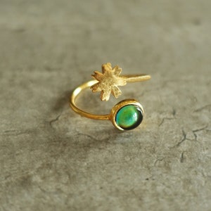 Peut inclure: Une bague en or avec une pierre verte irisée et un délicat motif de fleur. La bague est ouverte et réglable.