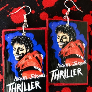 May include: A pair of earrings featuring a wood-like design with a black and white image of Michael Jackson from the Thriller album cover. The earrings are red and black with the text "Michael Jackson's Thriller" on the bottom.