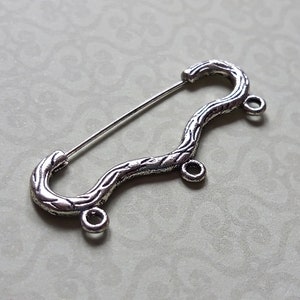May include: Silver-toned metal safety pin with a decorative, twisted design. The pin has three loops on the side.