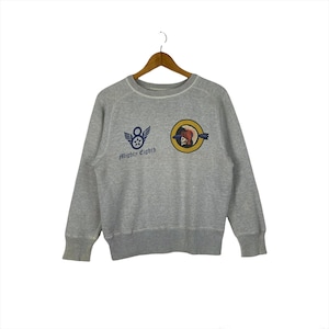 May include: A heather gray sweatshirt with the text "Mighty Eighth" and two patches. One patch features a star with wings, and the other shows a skull in a pilot's helmet. The sweatshirt is hanging on a wooden hanger.