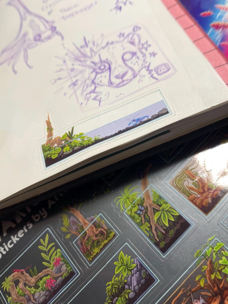 May include: A sketchbook with purple sketches of a flower and a cat-like face, and a sticker sheet featuring miniature terrarium designs with plants, trees, and a blue butterfly. The stickers are labeled "Stickers by Art".