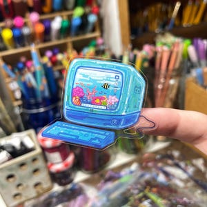 Peut inclure: Autocollant transparent repr&eacute;sentant un ordinateur r&eacute;tro avec une sc&egrave;ne d'aquarium &agrave; l'int&eacute;rieur du moniteur. L'autocollant a un clavier et un moniteur bleus, avec un poisson noir et jaune, du corail et d'autres cr&eacute;atures aquatiques.