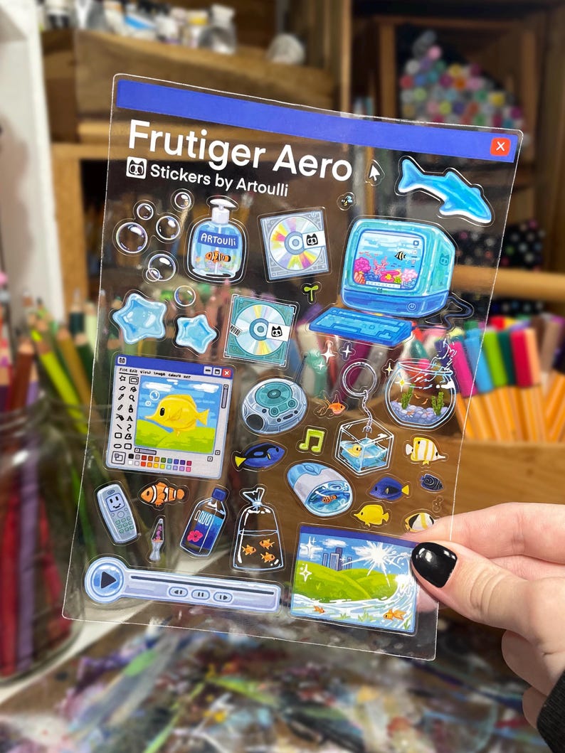 Peut inclure: Une planche d'autocollants transparente avec des motifs Frutiger Aero. Les autocollants comprennent un ordinateur r&eacute;tro, des CD, des poissons, des bulles et un bouton de lecture. Le texte "Frutiger Aero Stickers by Artoulli" est imprim&eacute; en haut.