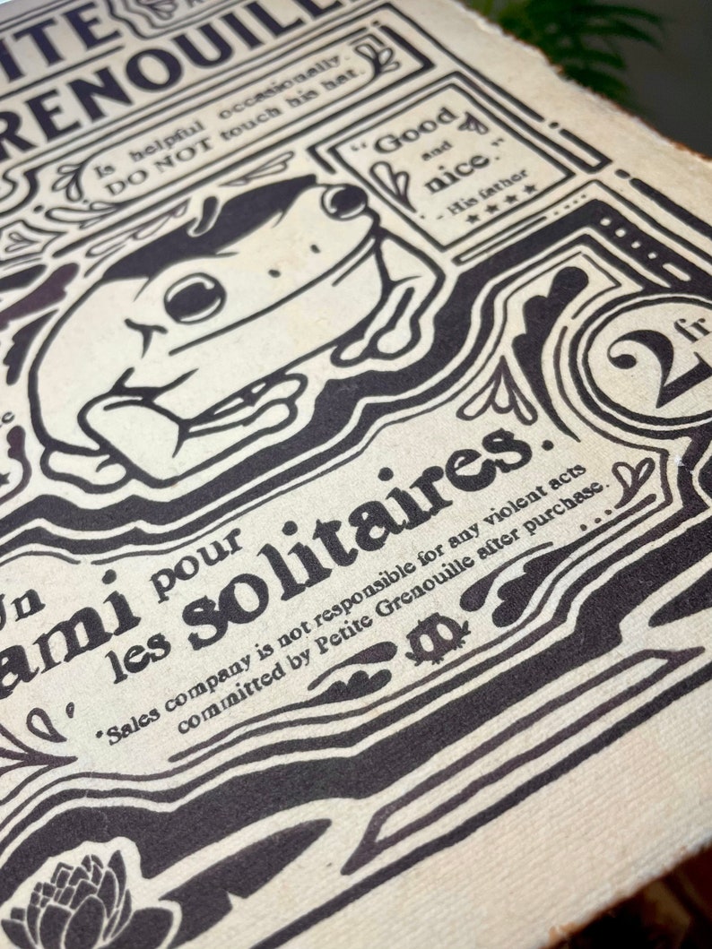 Może przedstawiać: Czarno-biała ilustracja żaby z tekstem "Petite Grenouille" i "Ami pour les solitaires" na kremowym tle. Tekst brzmi "Sales company is not responsible for any violent acts committed by Petite Grenouille after purchase."