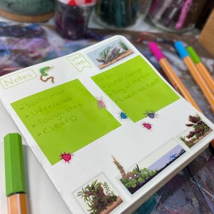 May include: Open notebook with green sticky notes and small stickers. The notes read "Waterproof, UV resistant, Tough stick, Clear." The "To do" list includes "Water change, Buy all the fish, Love all the fish." Colorful pens and jars are in the background.