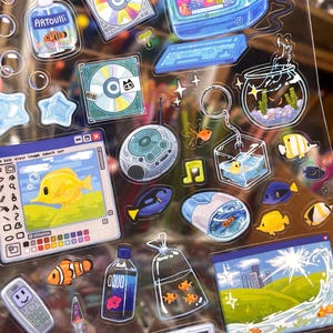Peut inclure: Une planche d'autocollants color&eacute;s repr&eacute;sentant la vie aquatique et la technologie r&eacute;tro. Les motifs comprennent un ordinateur, des CD, un aquarium, une lampe &agrave; lave et une bouteille avec l'inscription "AQUO". Les autocollants ont une finition brillante et sont de formes vari&eacute;es.