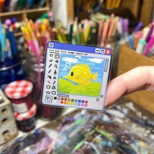 Peut inclure: Un autocollant transparent repr&eacute;sentant un poisson jaune dans un cadre de fen&ecirc;tre bleu, rappelant une interface informatique. L'autocollant comprend le texte "File Edit View Image Colours Help" et une palette de couleurs.