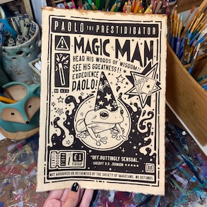 May include: A vintage-style poster advertising a magic show featuring a frog wearing a wizard's hat. The poster is titled "Paolo the Prestidigitator Magic Man" and includes the text "Hear his words of wisdom! See his greatness!! Experience Paolo!" The poster also includes a price of $1 and the text "Off-duttingly Sensual" with the name "Sherriff D.D. Johnson" and five stars. The poster also includes the text "Not approved or recognized by the Society of Magicians. No refunds."