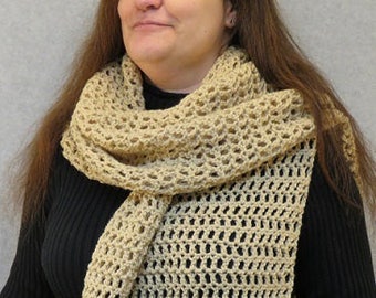 May include: A beige crochet scarf with a loose, open weave pattern. The scarf is draped around the neck of a person wearing a black shirt.