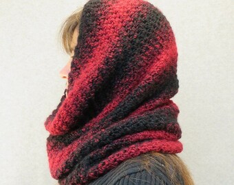May include: A black and red cowl neck scarf with a crocheted texture. The scarf is folded over and worn around the neck.