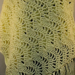 May include: A crocheted shawl in a pale yellow color with a delicate, lacy pattern and a fringe border.