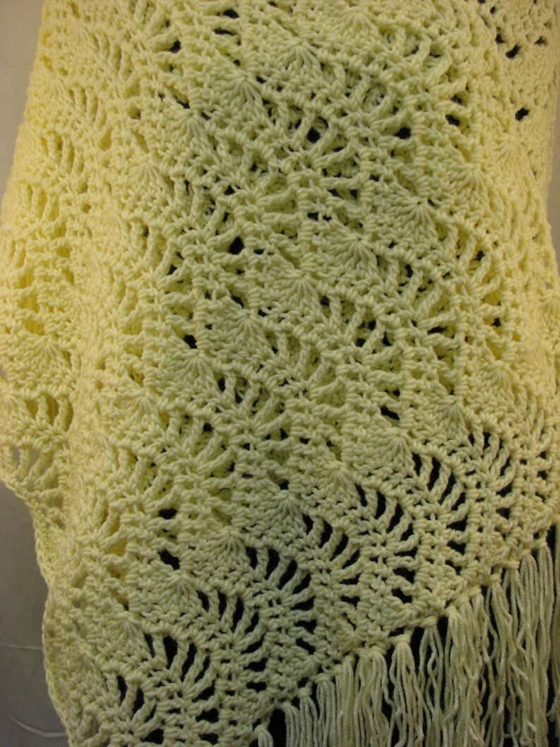 May include: A crocheted shawl in a pale yellow color with a delicate, lacy pattern and a fringe border.