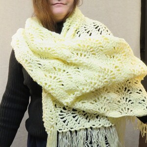 May include: A woman wearing a pale yellow crocheted shawl with fringe. The shawl is draped around her shoulders and neck.