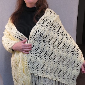 May include: A pale yellow crocheted shawl with a delicate openwork pattern and fringe. The shawl is draped over a person's shoulders.