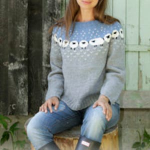 Könnte beinhalten: Ein grauer und blauer Strickpullover mit einem weißen Schaf-Muster. Der Pullover hat einen runden Ausschnitt und lange Ärmel.