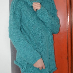 Könnte beinhalten: Ein tealblauer Strickpullover mit einem Rollkragen und langen Ärmeln.
