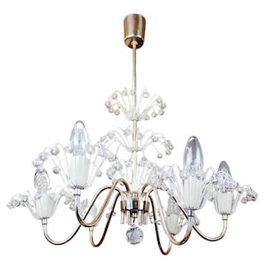May include: A silver chandelier with clear glass crystals and white glass bulbs. The chandelier has a floral design and is suspended from a silver chain.