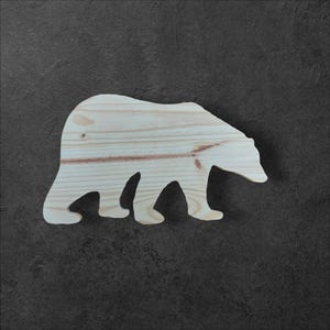 Peut inclure: Une découpe en bois d'un ours en position de marche. L'ours est en bois brun clair et est une silhouette simple.
