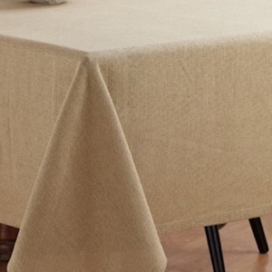 May include: A beige rectangular tablecloth with a subtle woven texture. The tablecloth is draped over a wooden table with a black chair.