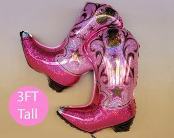 Op de afbeelding: Twee grote roze cowboylaarzen in de vorm van ballonnen met een glinsterende afwerking en stermotieven. De ballonnen zijn 91 cm hoog.