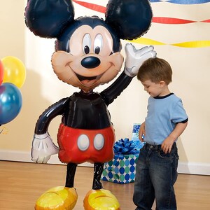 Puede incluir: Un gran globo de Mickey Mouse negro y rojo con un guante blanco. El globo est&aacute; de pie sobre un suelo de madera y un ni&ntilde;o peque&ntilde;o est&aacute; de pie junto a &eacute;l.