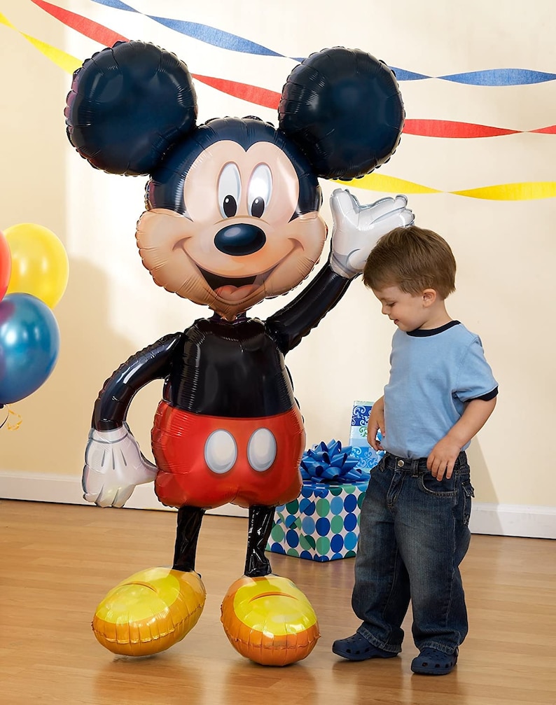 Puede incluir: Un gran globo de Mickey Mouse negro y rojo con un guante blanco. El globo est&aacute; de pie sobre un suelo de madera y un ni&ntilde;o peque&ntilde;o est&aacute; de pie junto a &eacute;l.