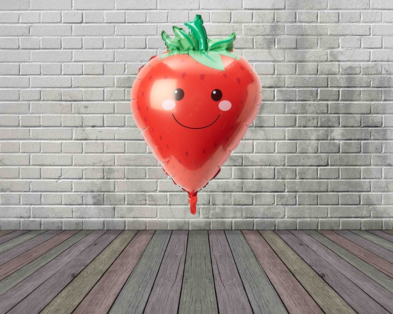 May include: A red and green foil balloon shaped like a strawberry with a smiling face.