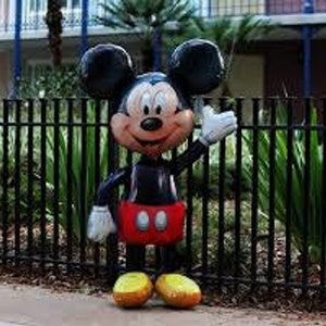Puede incluir: Un gran globo de Mickey Mouse negro y rojo con una gran sonrisa y guantes blancos. El globo est&aacute; de pie frente a una valla de metal negro.