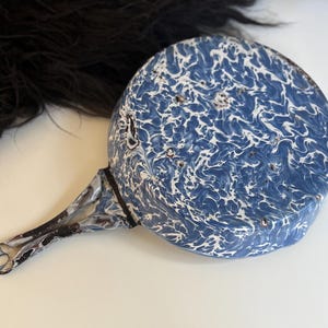 May include: A vintage blue and white enamel saucepan with a long handle. The pan has a speckled pattern and a metal handle. A classic kitchen item.